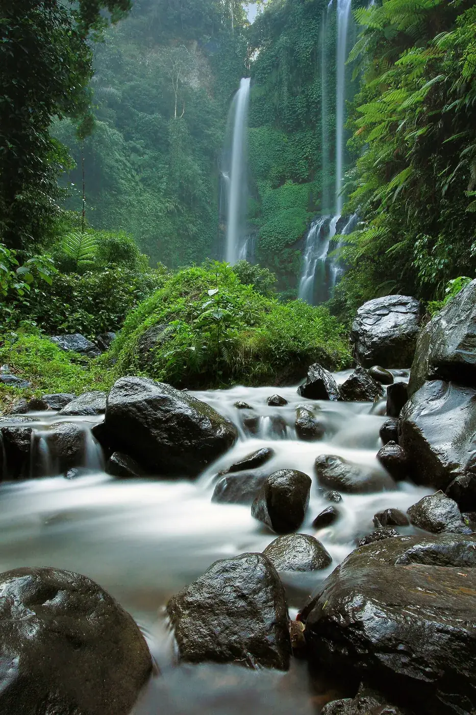 De hoge Sekumpulwatervallen achter rotsen in de rivier